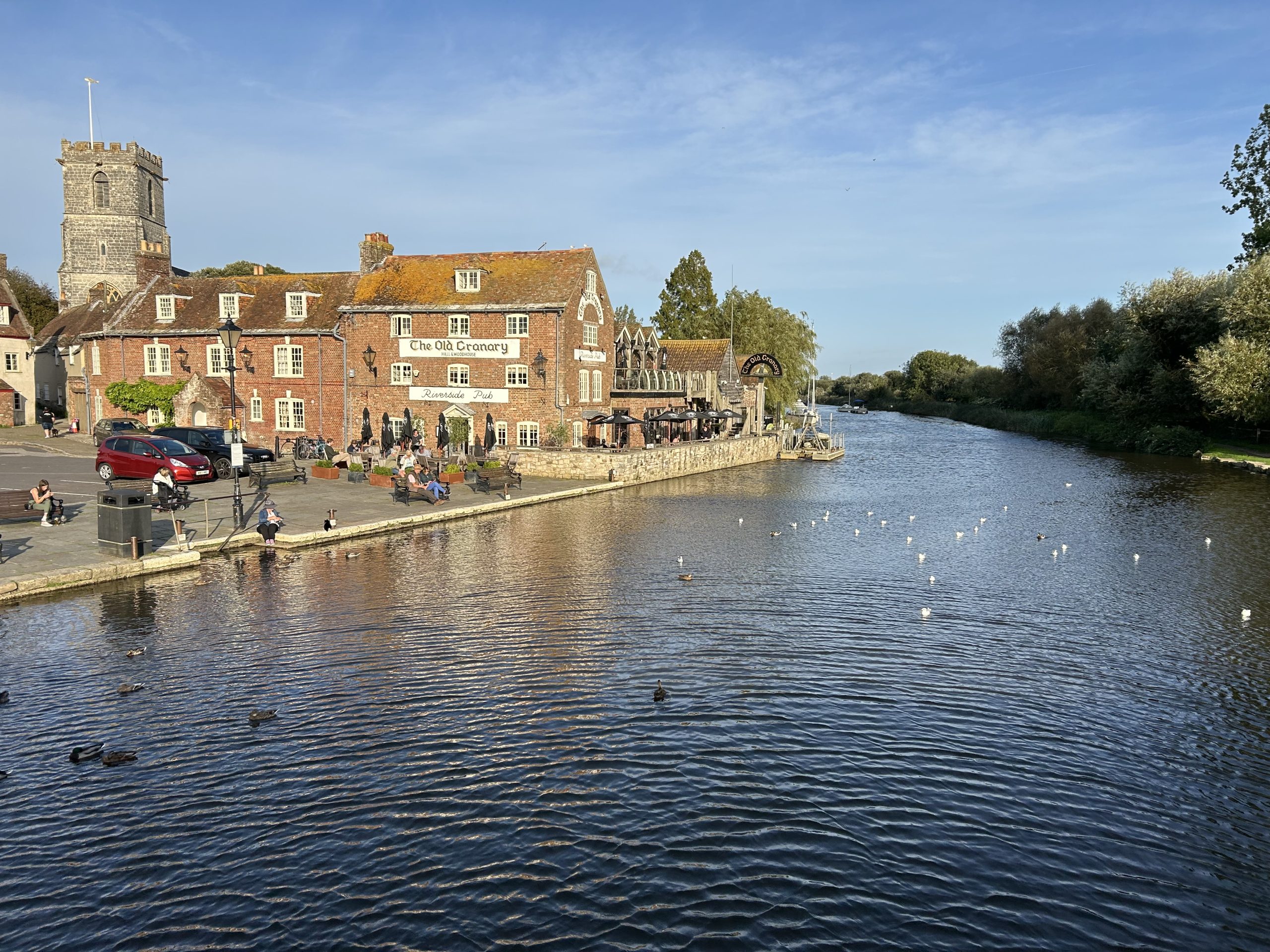 A photograph of a pretty old town, with a church tower, on the banks of a wide river.