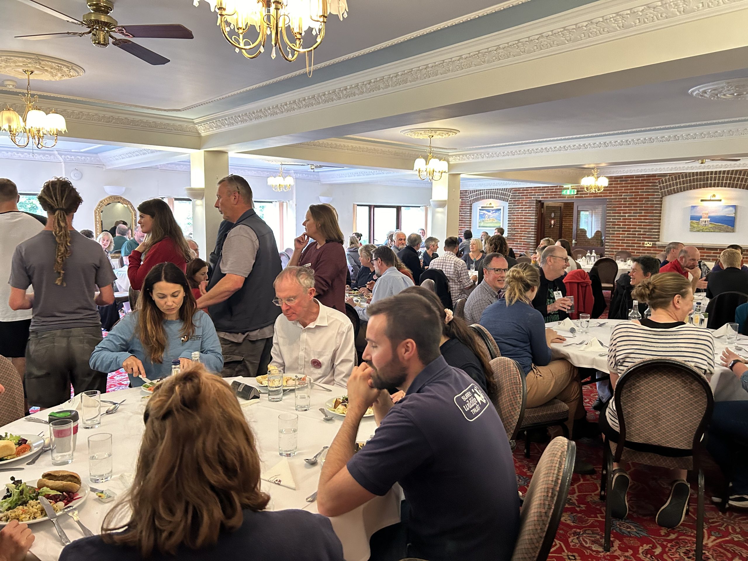 A photograph of many people in conversation around dinner tables laid out in a dining room.