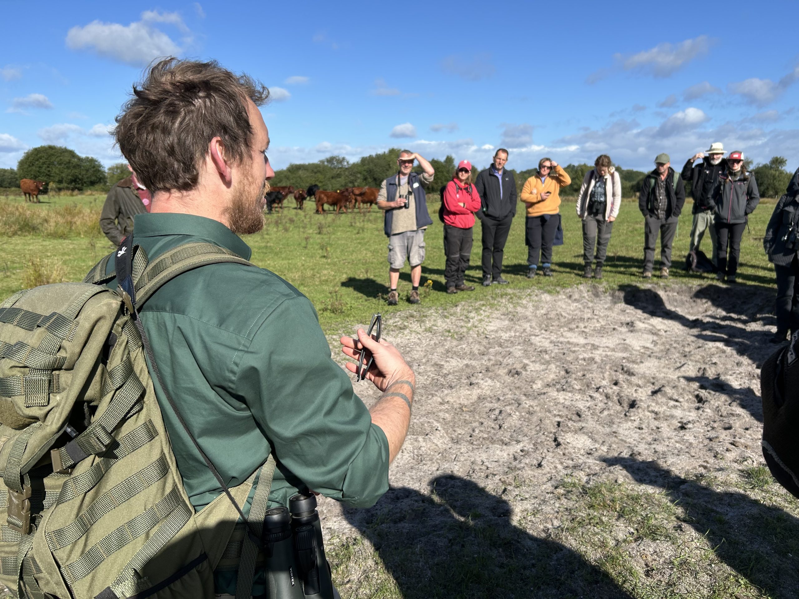 Photo of people on a fine day. They are looking at bare ground, where there is sandy soil.